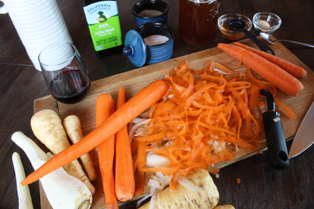 Peeled carrots and parsnips sit on a wooden cutting board before being roasted with maple syrup and extra virgin olive oil.