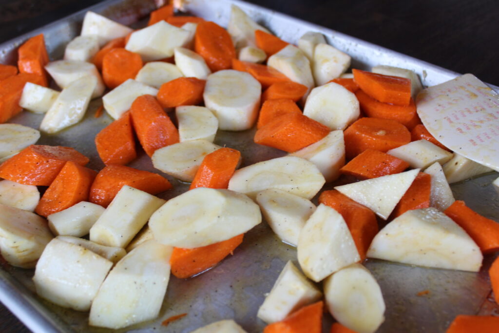 A sheet pan with seasoned parsnips and carrots waits to go in the oven. 
