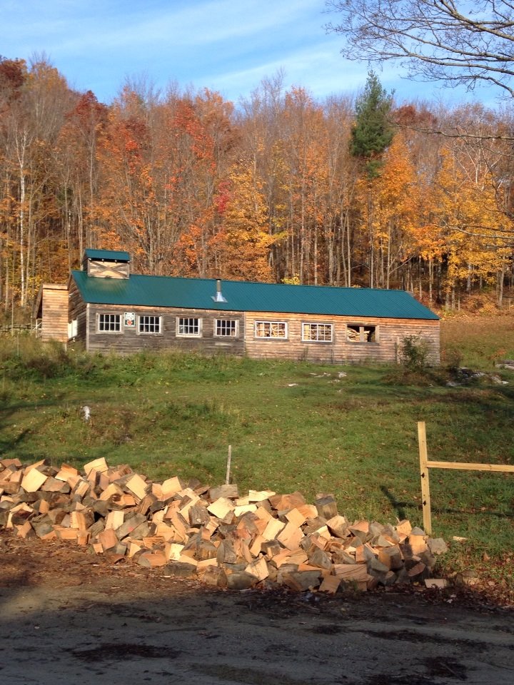 A pile of wood waits at the foot of a hill to be loaded up and stacked at a Vermont sugarhouse in the autumn months. Beautiful foliage dots the skyline. A sugarmakers work is never done. 