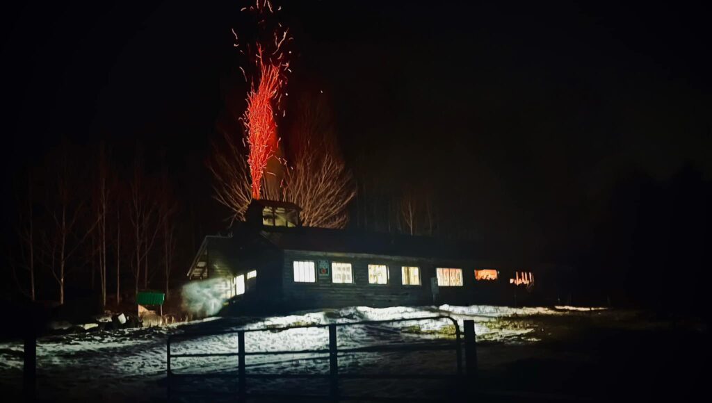 A Vermont sugar house with smoke and embers billowing from its chimney during a night of boiling during maple sugaring season and March maple month in New England. 