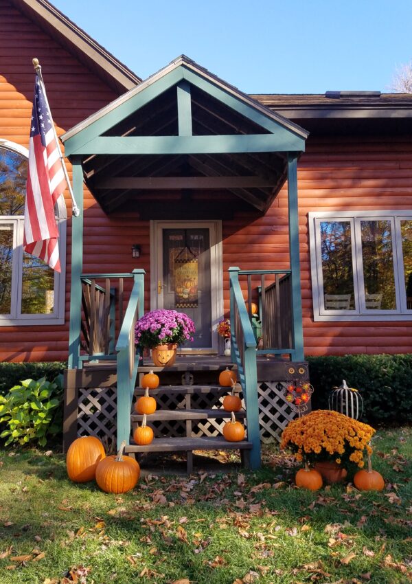 A rustic log cabin has its porch decorated with mums, pumpkins and other items for Halloween in New England