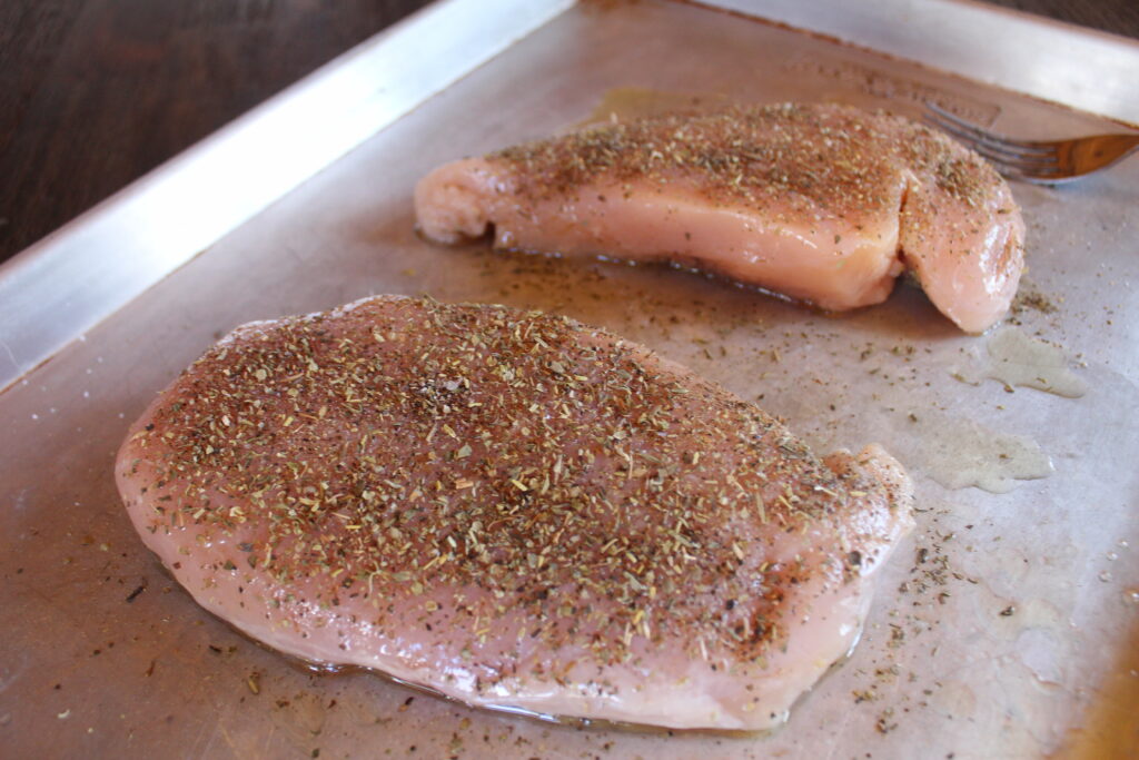 Chicken breasts on an oiled rimmed baking sheet with Italian seasoning before being roasted