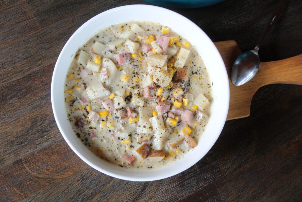 The best ham, potato and corn chowder. A bowl of warm ham, potato and corn chowder is dished out and ready to be served. A wide ceramic bowl shows off its beauty and color with a silver spoon waiting to dig in.