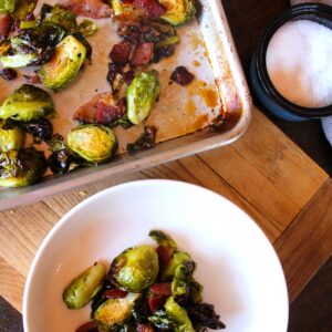 A white ceramic bowl filled with maple roasted brussels sprouts with bacon