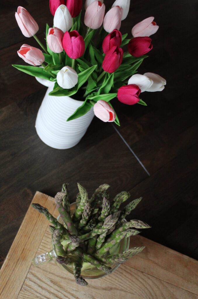 Trimmed asparagus sits in water alongside a white ceramic vase of lifelike tulips, before being roasted in the oven with simple seasonings