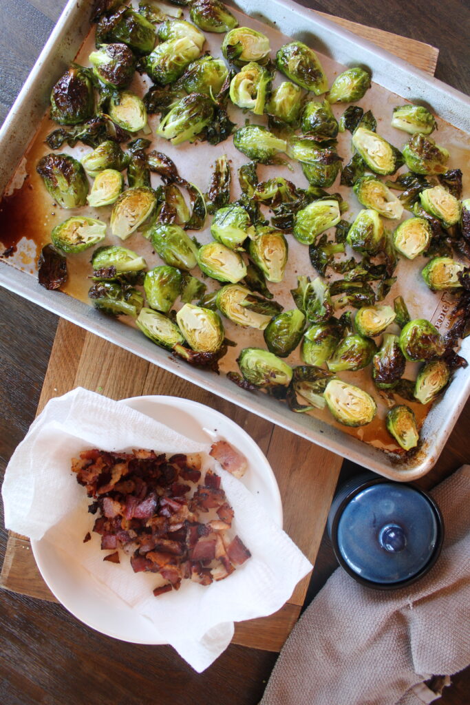 Roasted maple brussels sprouts on a baking sheet before cut, crispy bacon is added to the top. 