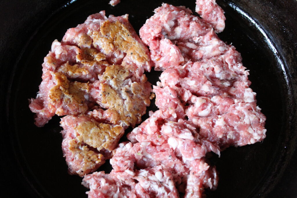 Ground Italian sweet sausage being browned in a cast iron pan