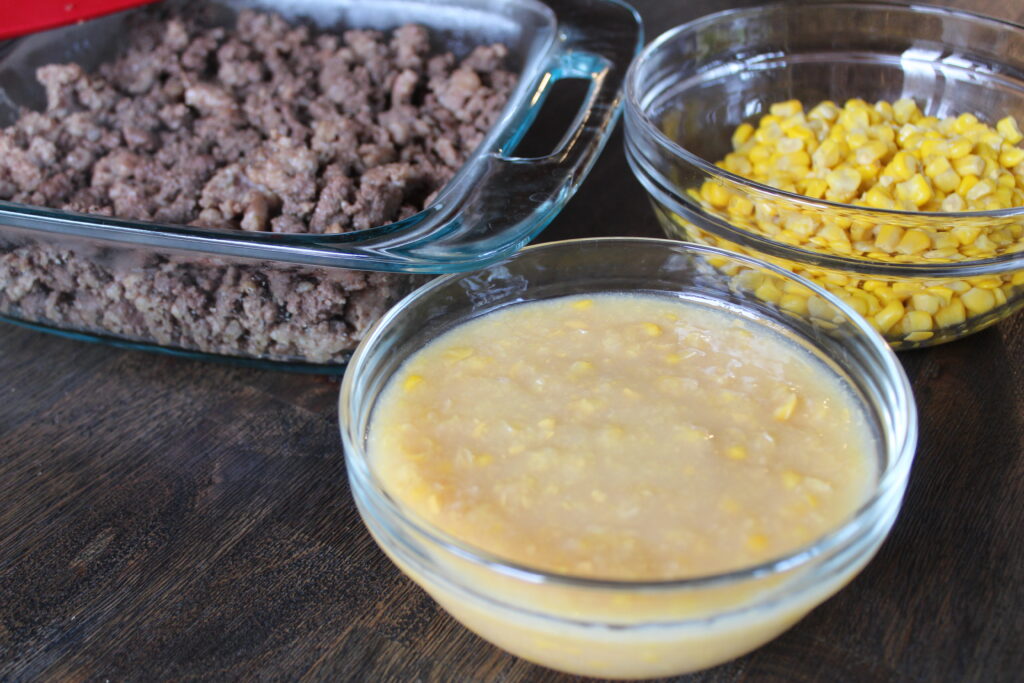 Creamed corn and whole kernel corn are ready to be layered on top of browned ground beef and Italian sausage