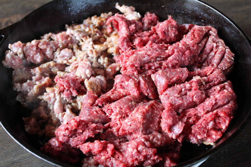 Ground Italian sweet sausage and ground beef being browned together in a cast iron pan